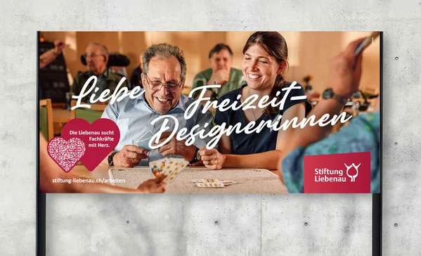 Werbeplakat: Eine lächelnde junge Frau und ein älterer Mann spielen Karten in einer Gruppe; freundliche Betreuungsszene mit Schriftzug Liebe Freizeit-Designerinnen und Logo der Stiftung Liebenau.